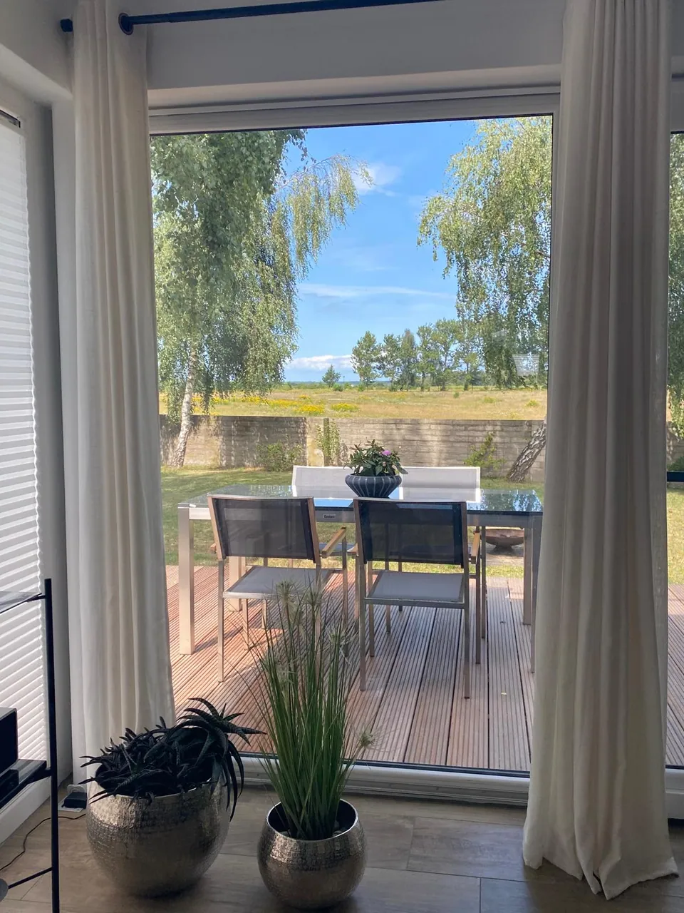 Blick durch bodentiefe Fenster auf die Terrasse und die Wiese