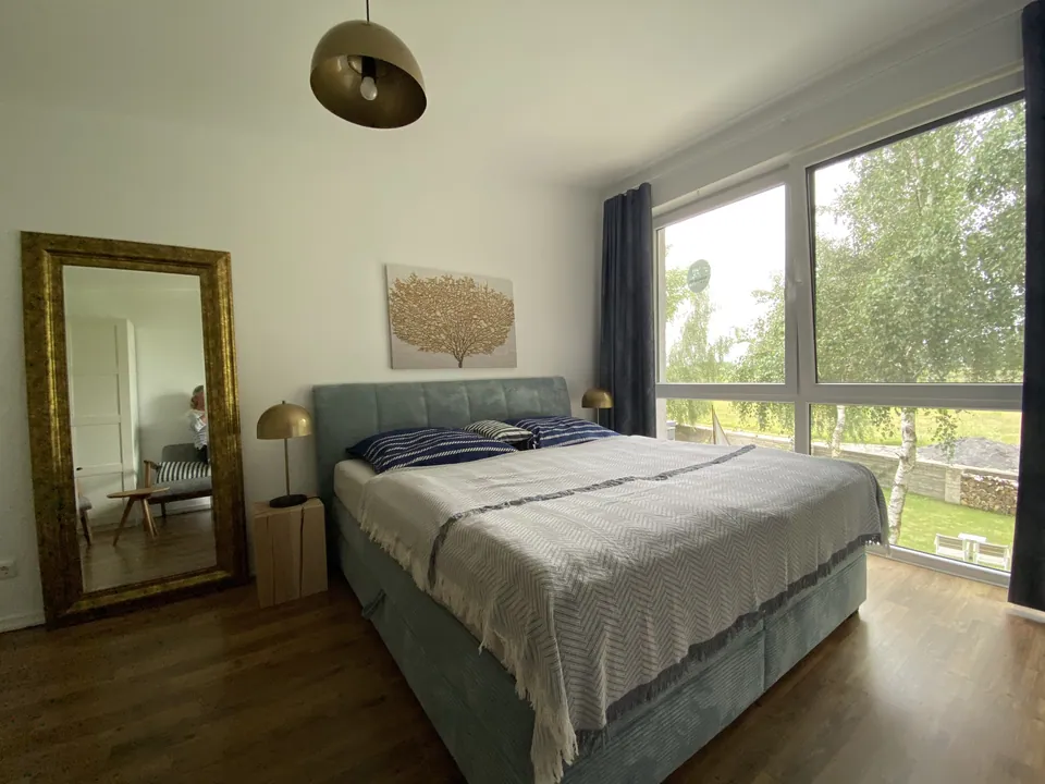 Boxspringbett in blauem Stoff vor dem bodentiefen Fenster