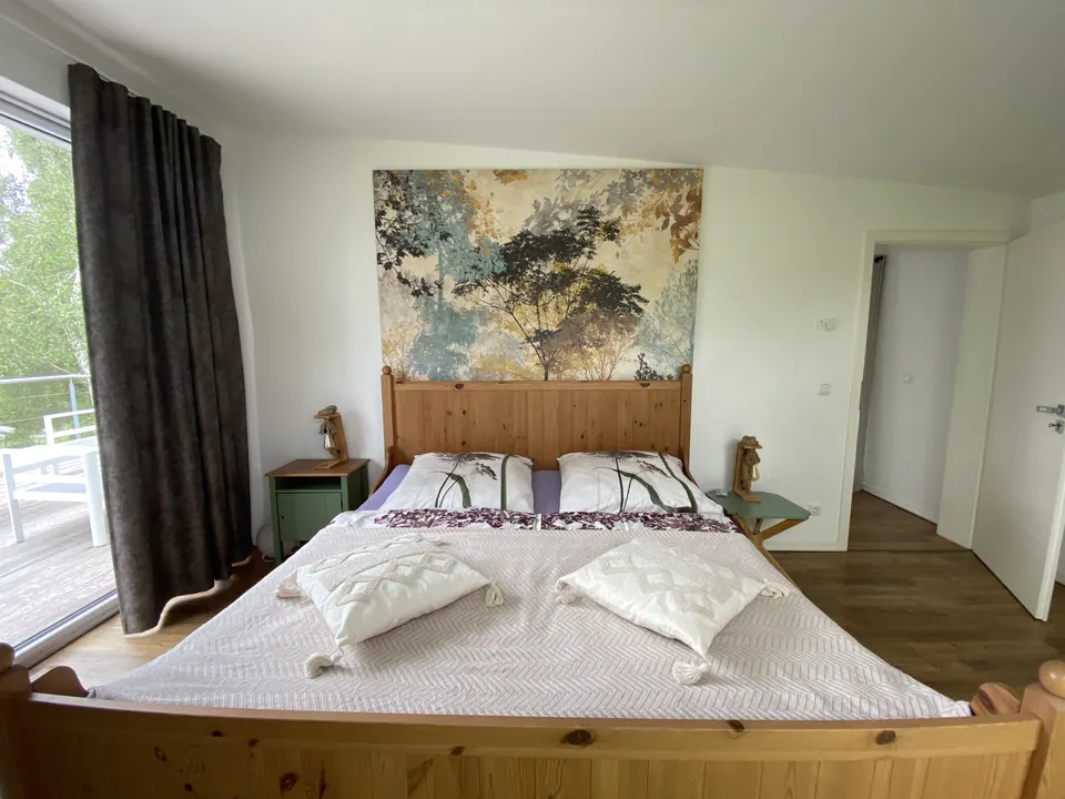 Schlafzimmer mit Holzbett, Wandbild und Zugang zur Terrasse