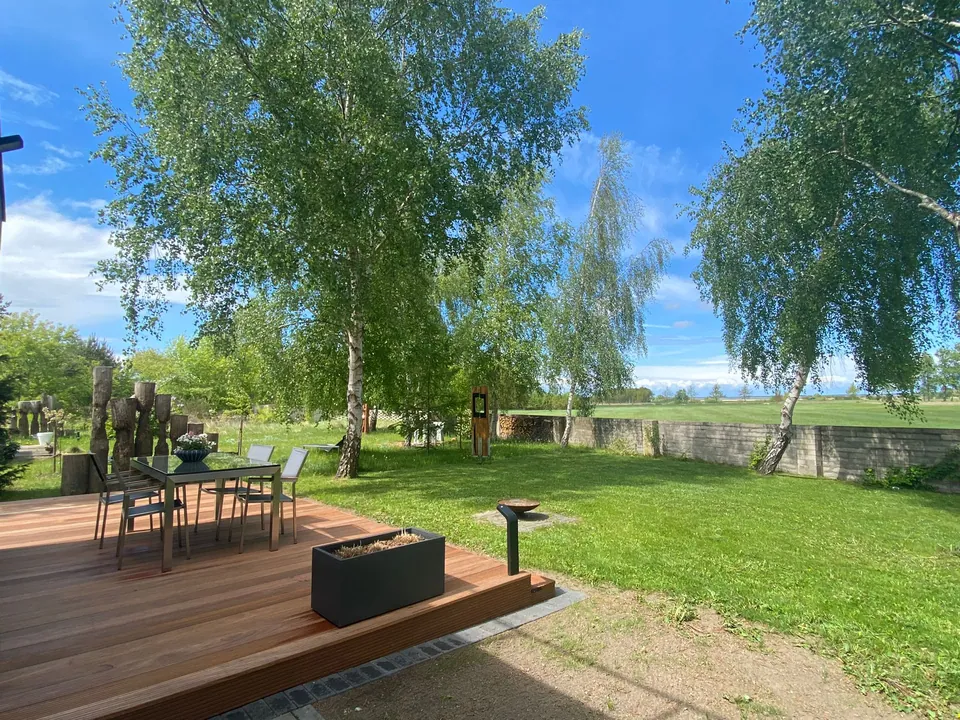 Holzterrasse mit Esstisch und Feuerschale, dahinter die Wiese und weiter Himmel