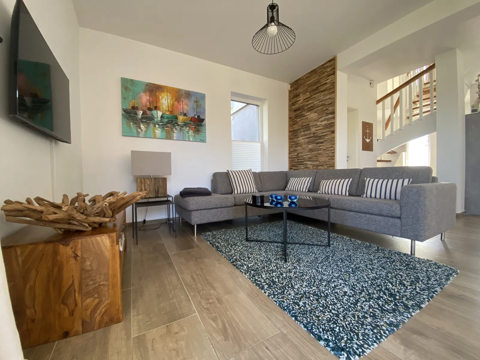 Wohnzimmer mit grauem Ecksofa, Holztisch und Treppe zur oberen Etage